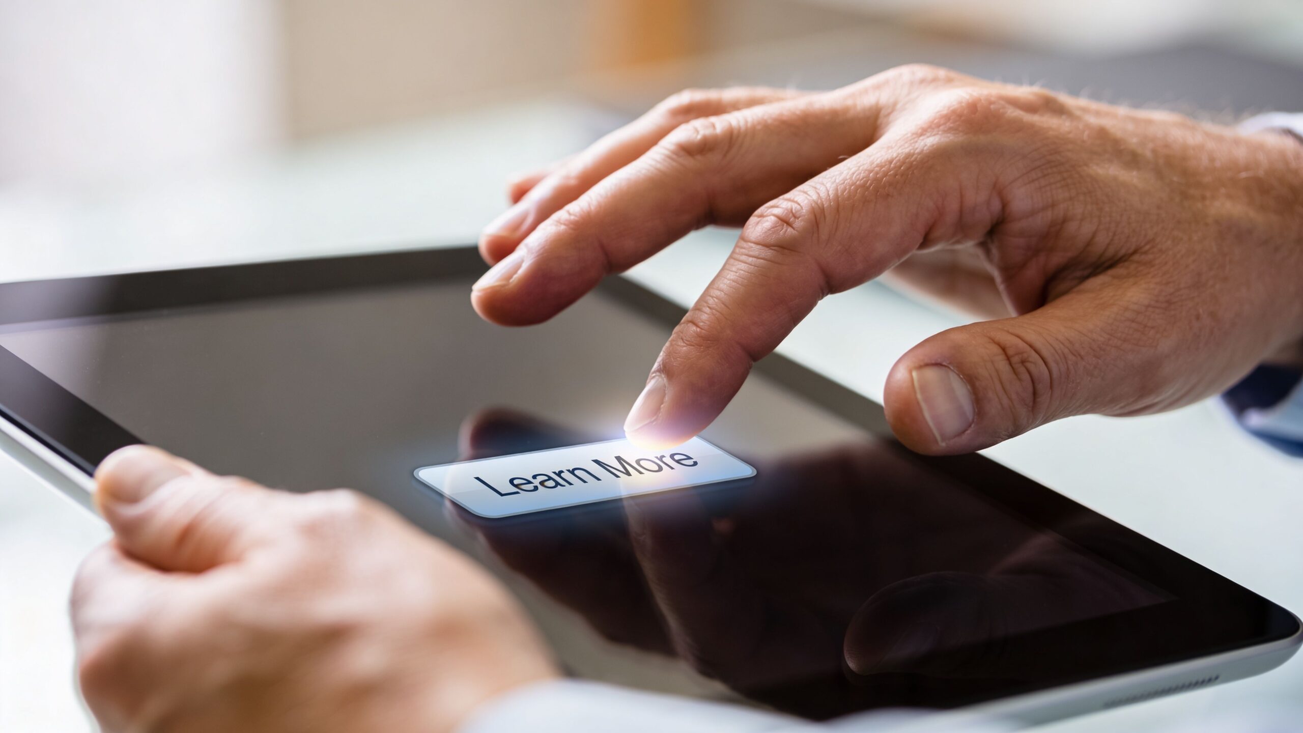 A close up view of a person using a finger to tap a learn more button on a tablet.