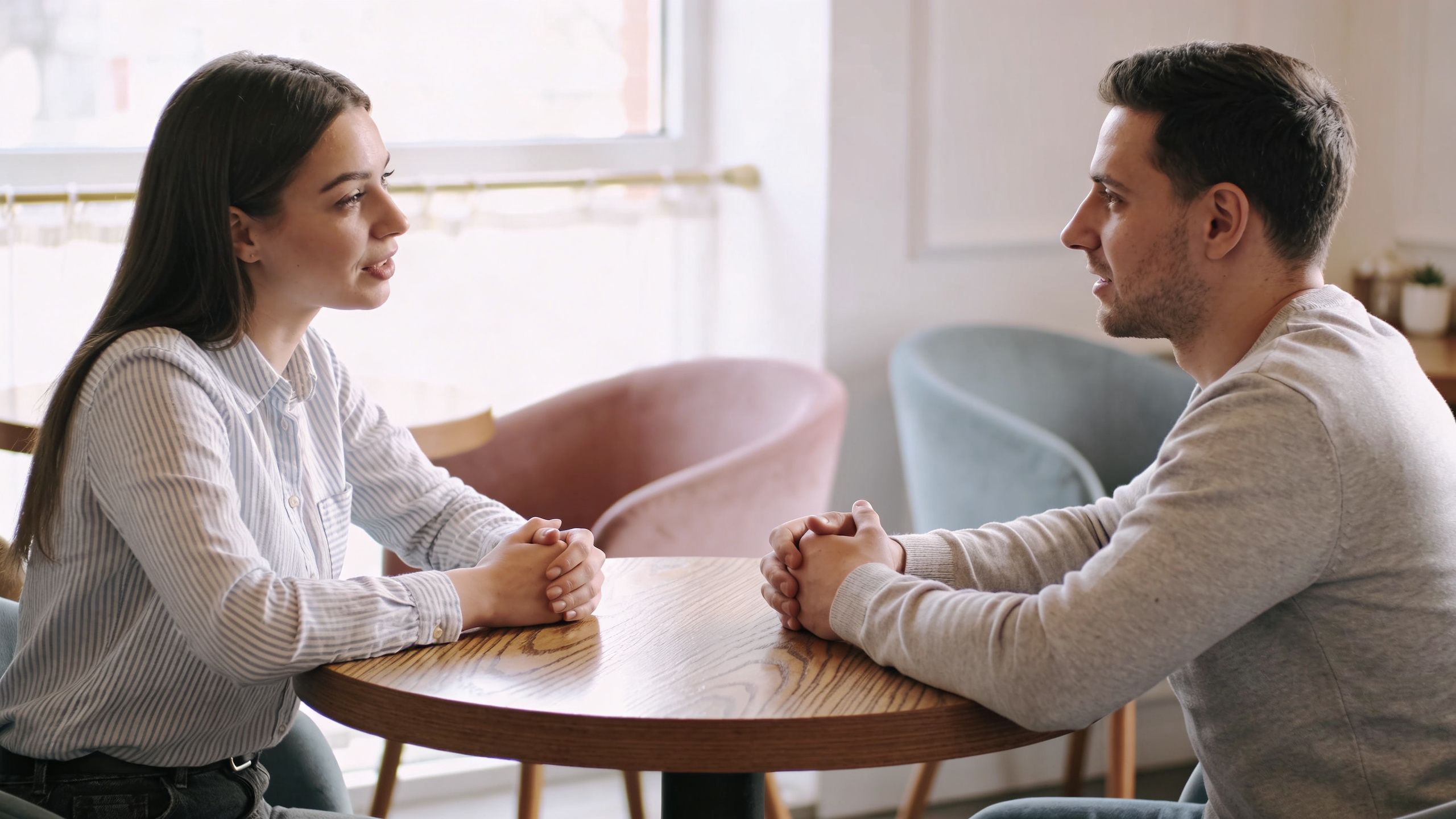 A man and a woman sitting at a wooden table in a cafe, engaged in a conversation.